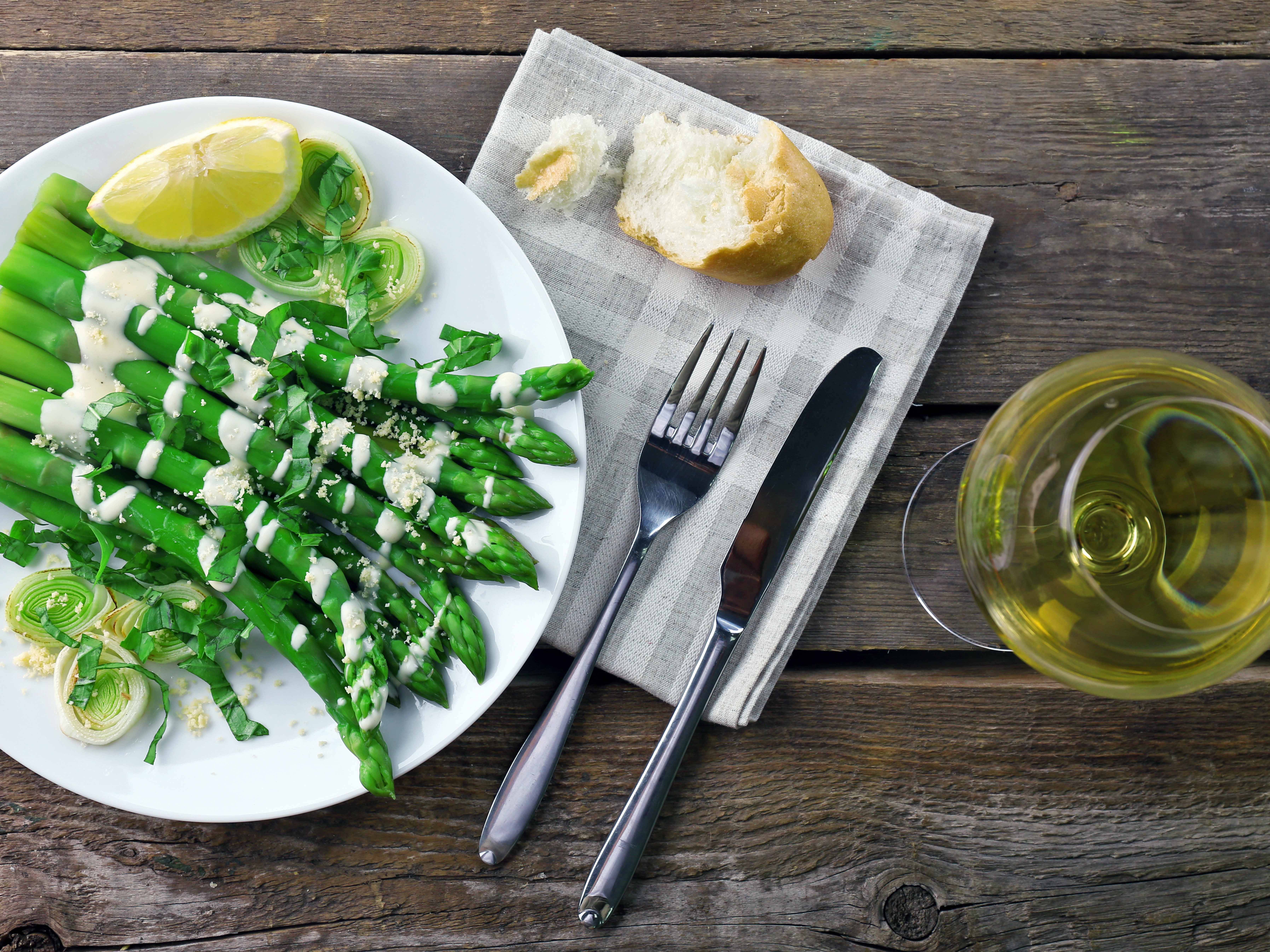 Spargel mit Sauce Hollandaise auf einem Teller und ein Glas Weißwein daneben. 